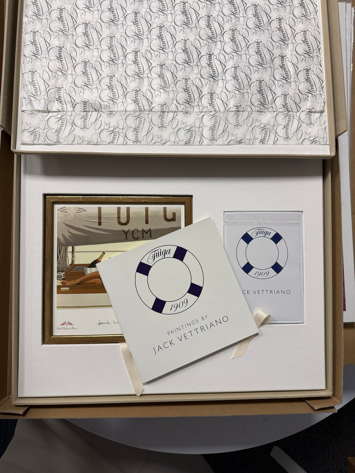 An open presentation box containing a framed artwork, a printed booklet and CD with a lifebuoy logo and the text 'Paintings by Jack Vettriano, - Tuiga 1909'